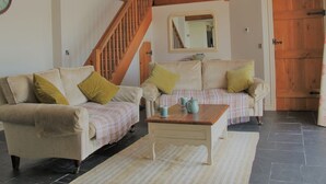 Un salon avec deux canapés, une table basse, un escalier, un miroir et une porte.