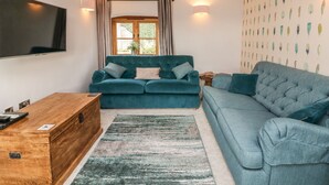 Un salon avec un canapé, une commode en bois, un téléviseur et une fenêtre avec des rideaux.