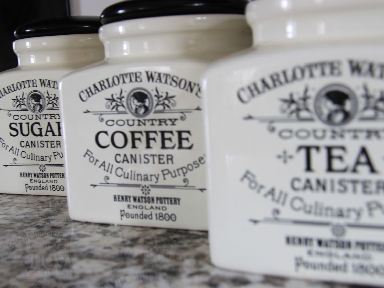 Three containers labeled 'Charlotte Watson's Country Sugar,' 'Country Coffee,' and 'Tea,' each with a black lid and a white body.