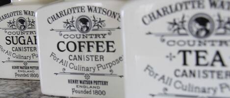 Three containers labeled 'Charlotte Watson's Country Sugar,' 'Country Coffee,' and 'Tea,' each with a black lid and a white body.