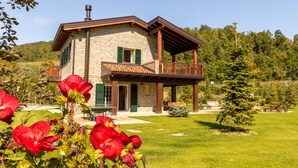 Une maison en pierre dotée d’un balcon, entourée d’une pelouse bien entretenue et de plantes en fleurs.