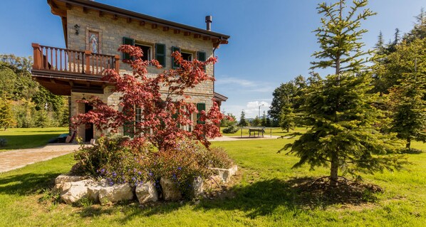 A stone building with a balcony, surrounded by a well-maintained lawn and trees.