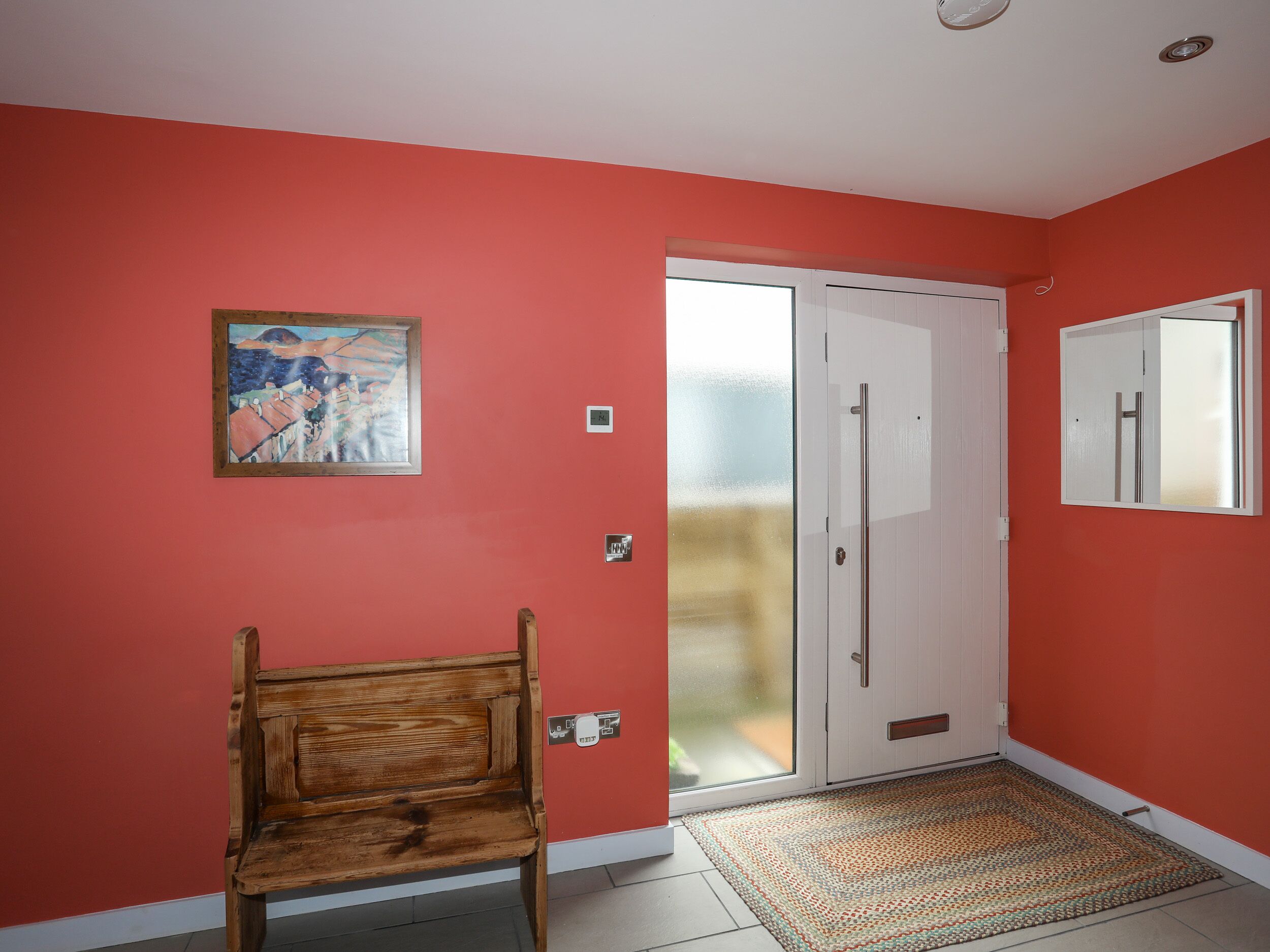 Una habitación con pared roja, un banco de madera, una puerta con panel de vidrio esmerilado y una alfombra pequeña.