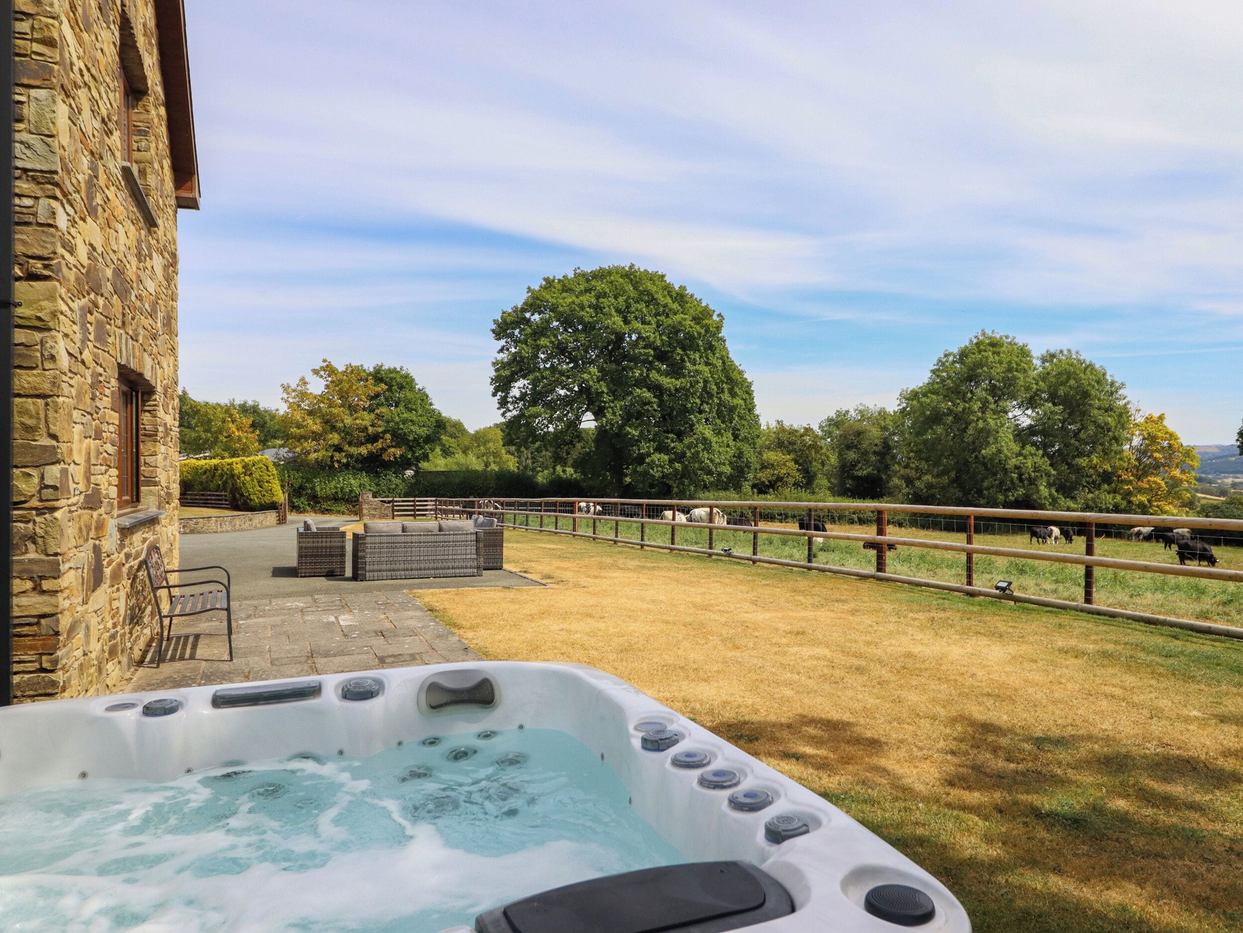 A stone building with a hot tub and a fenced area with cows.