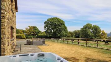A stone building with a hot tub and a fenced area with cows.
