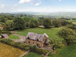 A stone building with a sloped roof, surrounded by a fenced property with a grassy field and trees.