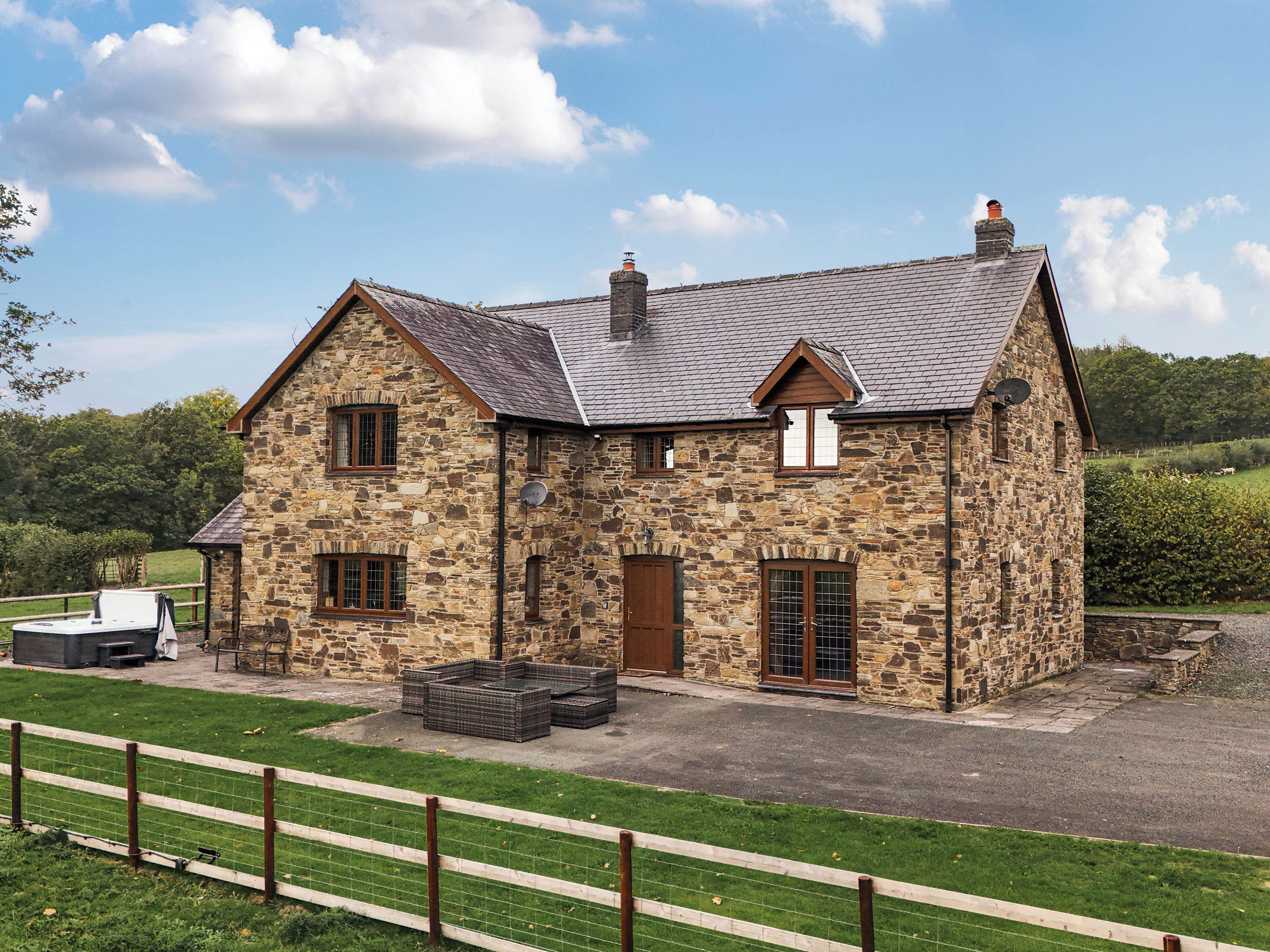 A stone house with a pitched roof, a chimney, and a fenced yard.