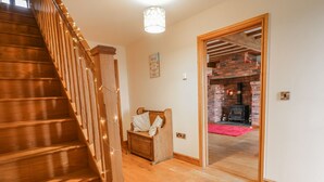 Una escalera de madera con luces cálidas, un banco de madera con cojines, y una chimenea de ladrillo al fondo.