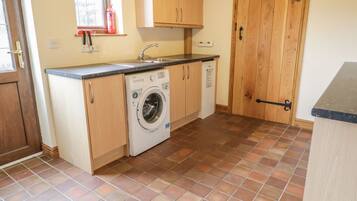A compact kitchen with a washing machine, wooden cabinets, a tiled floor, and a wooden door.