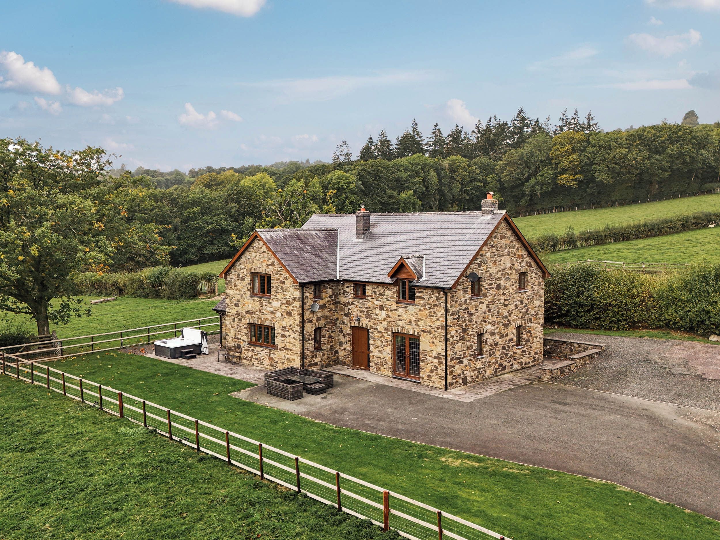 A stone farmhouse with a fenced yard and a gravel driveway.
