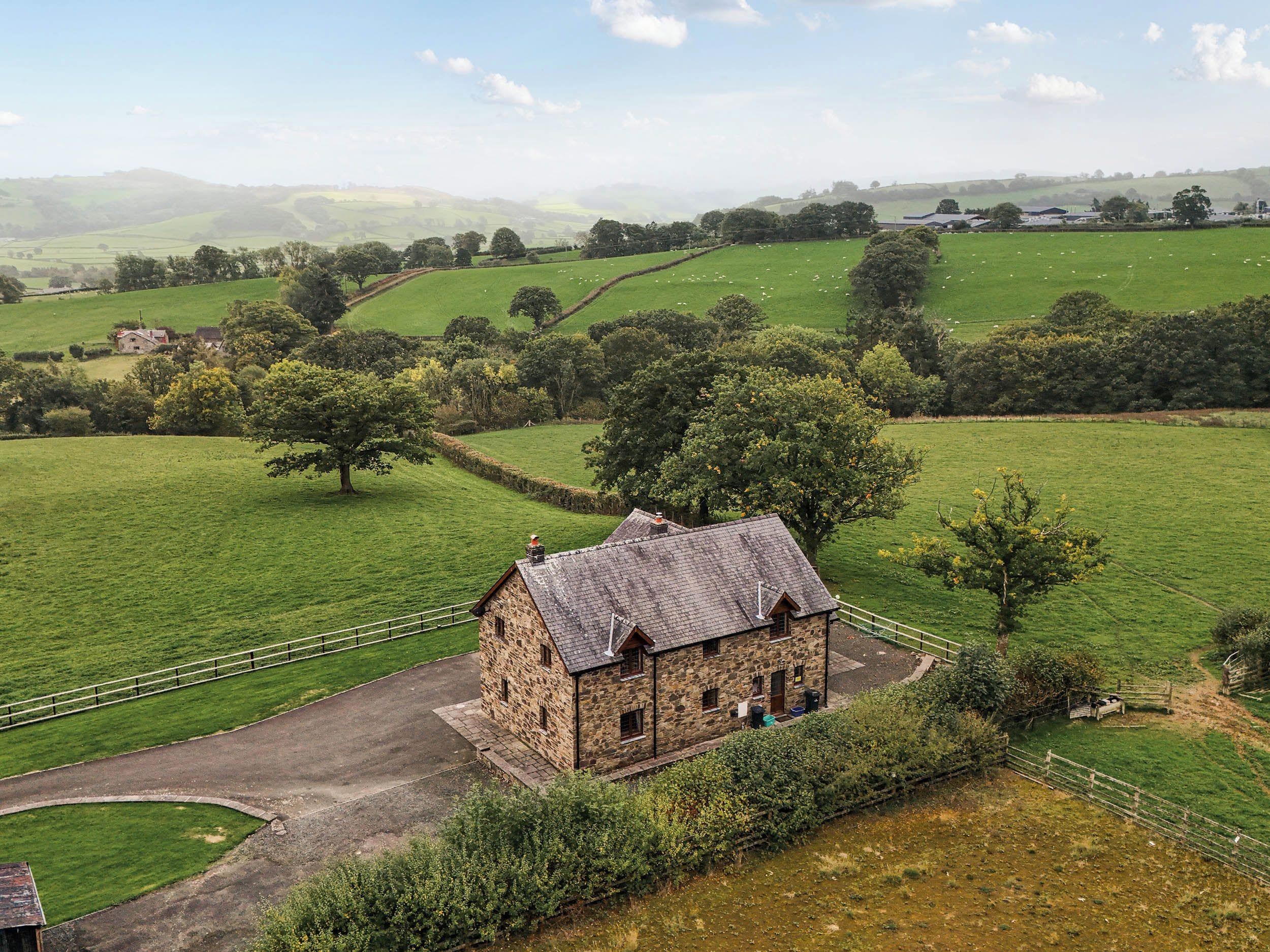 A stone building with a sloped roof, surrounded by green fields and trees.