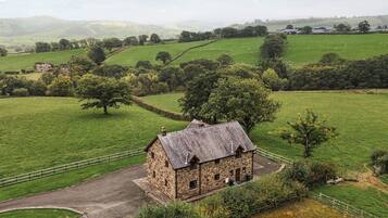 A stone building with a sloped roof, surrounded by green fields and trees.