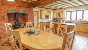 Una cocina amplia con chimenea de ladrillo, vigas de madera y una gran mesa de comedor rodeada de sillas.