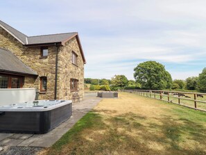 A stone building with a hot tub and a fenced area with cows. - Ty Berllan (Caersws)