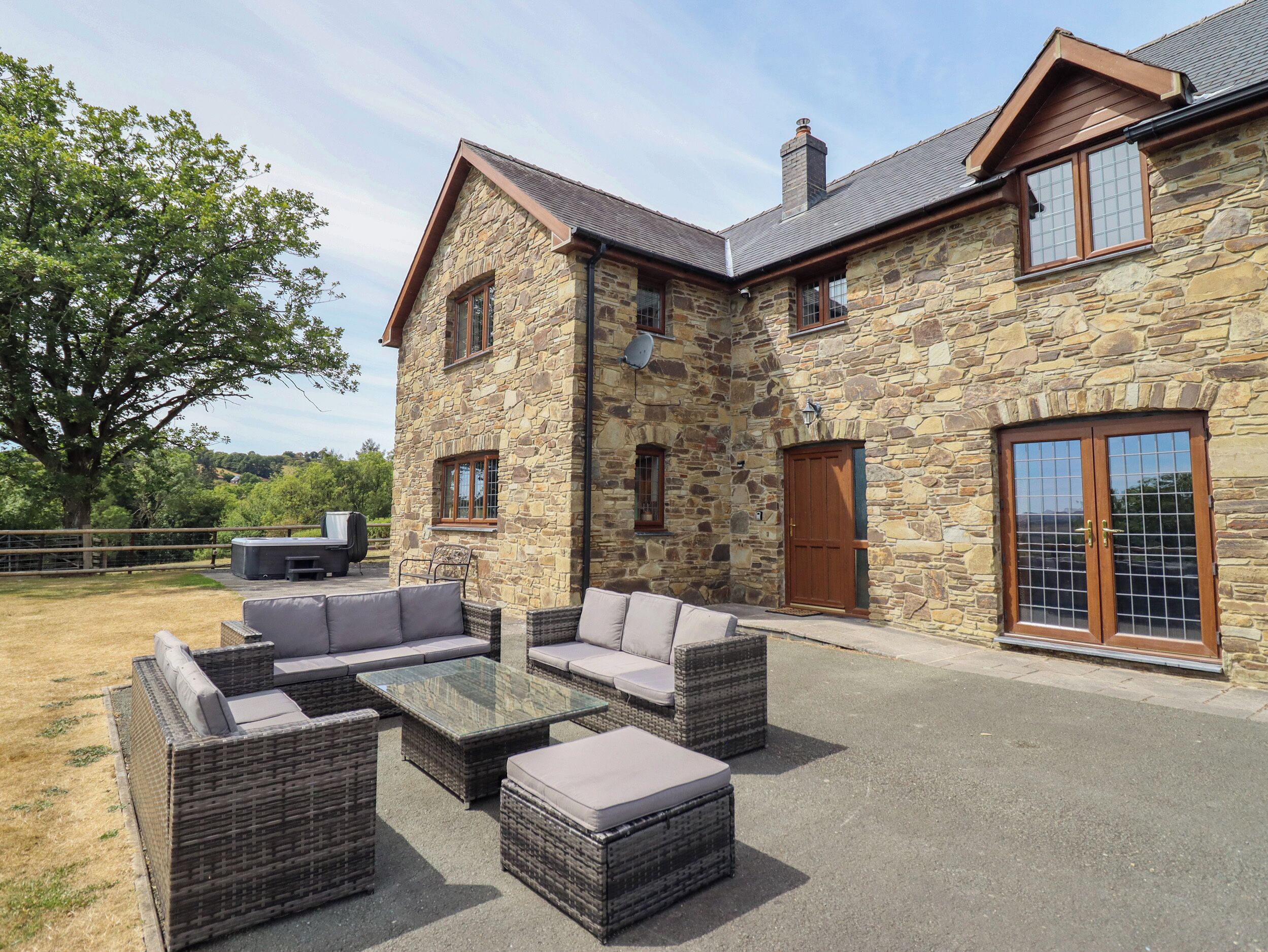 A stone house with a patio area featuring wicker furniture and a glass table.