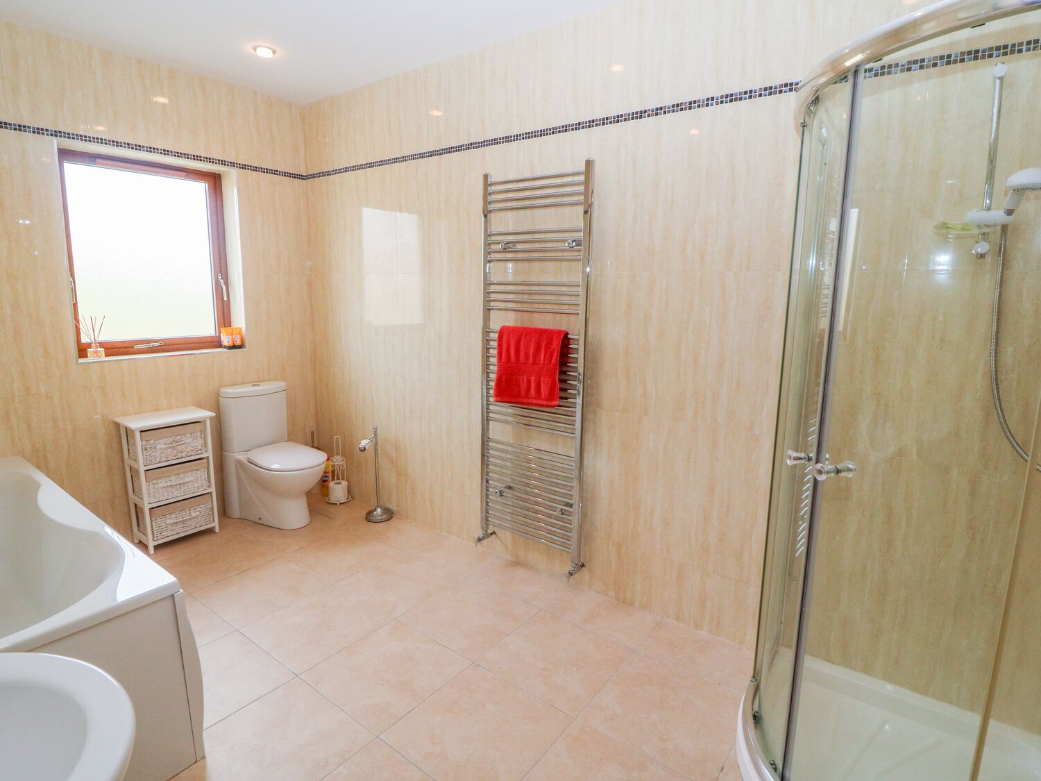 A modern bathroom with a glass shower enclosure, a white toilet, a bathtub, and a towel rack with a red towel.