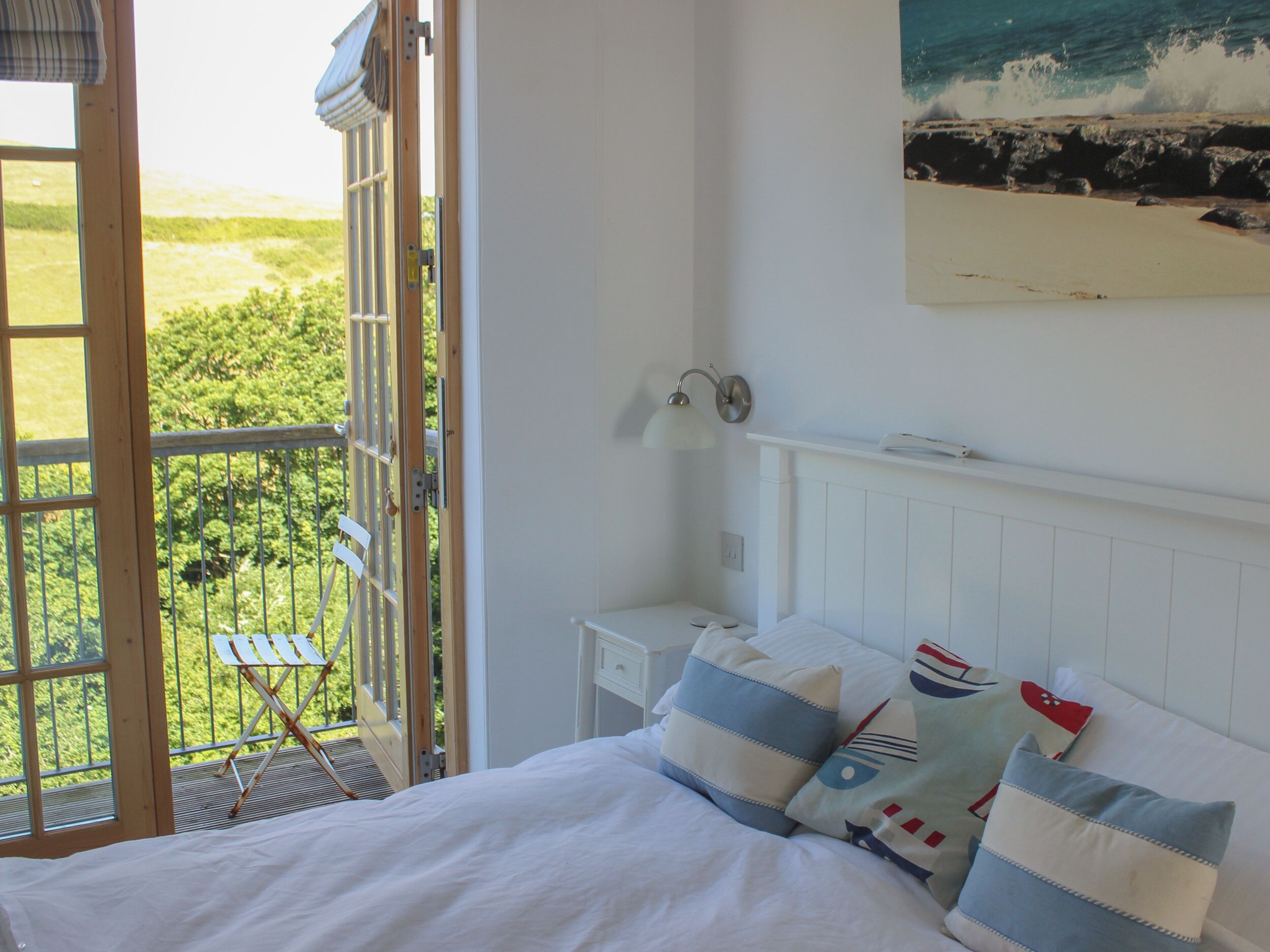 A bedroom with a bed, pillows, a nightstand, a lamp, and a view of the outdoors.