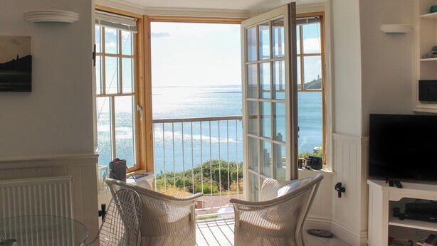 A room with a large bay window overlooking a body of water, a television, and a wicker chair.