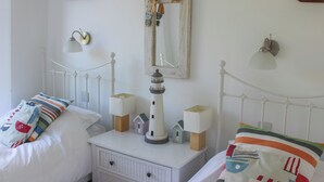 A bedroom with a white metal bed frame, two bedside tables with lamps, a small lighthouse model, and nautical-themed wall decorations.