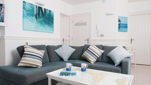 A living room with a grey sofa, striped pillows, a coffee table with a map, and a 'BEACH' sign on the wall.
