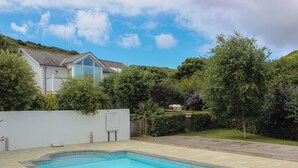 A swimming pool with a tiled deck, surrounded by a white wall and lush greenery.