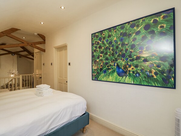 A bedroom with a large bed, a white door, and a painting of peacock feathers on the wall. - The Old Reading Room (Chipping Norton)