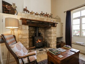 A cozy living room with a stone fireplace, a wooden mantel, and a chair with a patterned cushion. - The Old Reading Room (Chipping Norton)