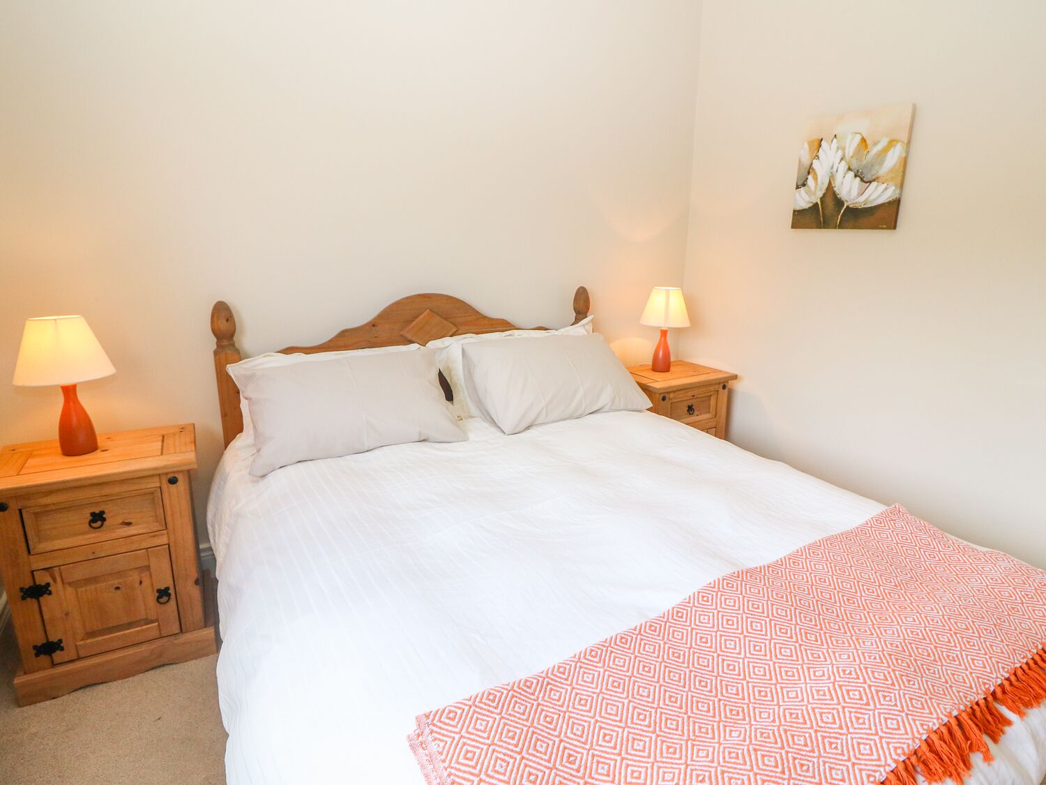 A neatly made bed with white bedding, two bedside tables with lamps, and a single wall-mounted painting.