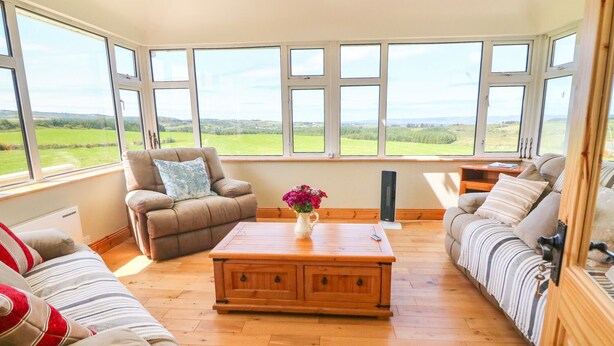 Un salón espacioso con ventanas amplias, una mesa de centro de madera y vistas al campo.
