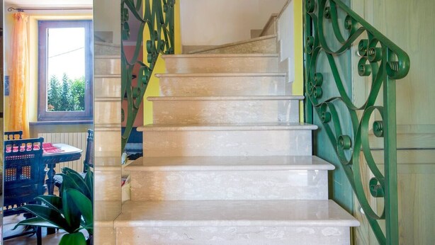 Un escalier avec des rampes en métal vert, donnant sur une pièce avec une fenêtre et une table.