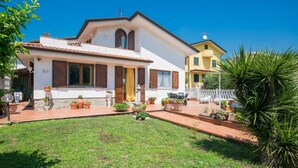 Une maison à deux étages avec un porche à l’avant, un petit jardin et un espace patio.