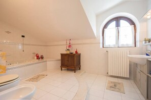 A bathroom with a bathtub, a wooden cabinet, a radiator, and a window with curtains. - JOIVY Shared Villa Nature&relax (Massarosa)