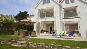 Una casa a due piani con un balcone, un'area salotto esterna e un muro in pietra in primo piano.