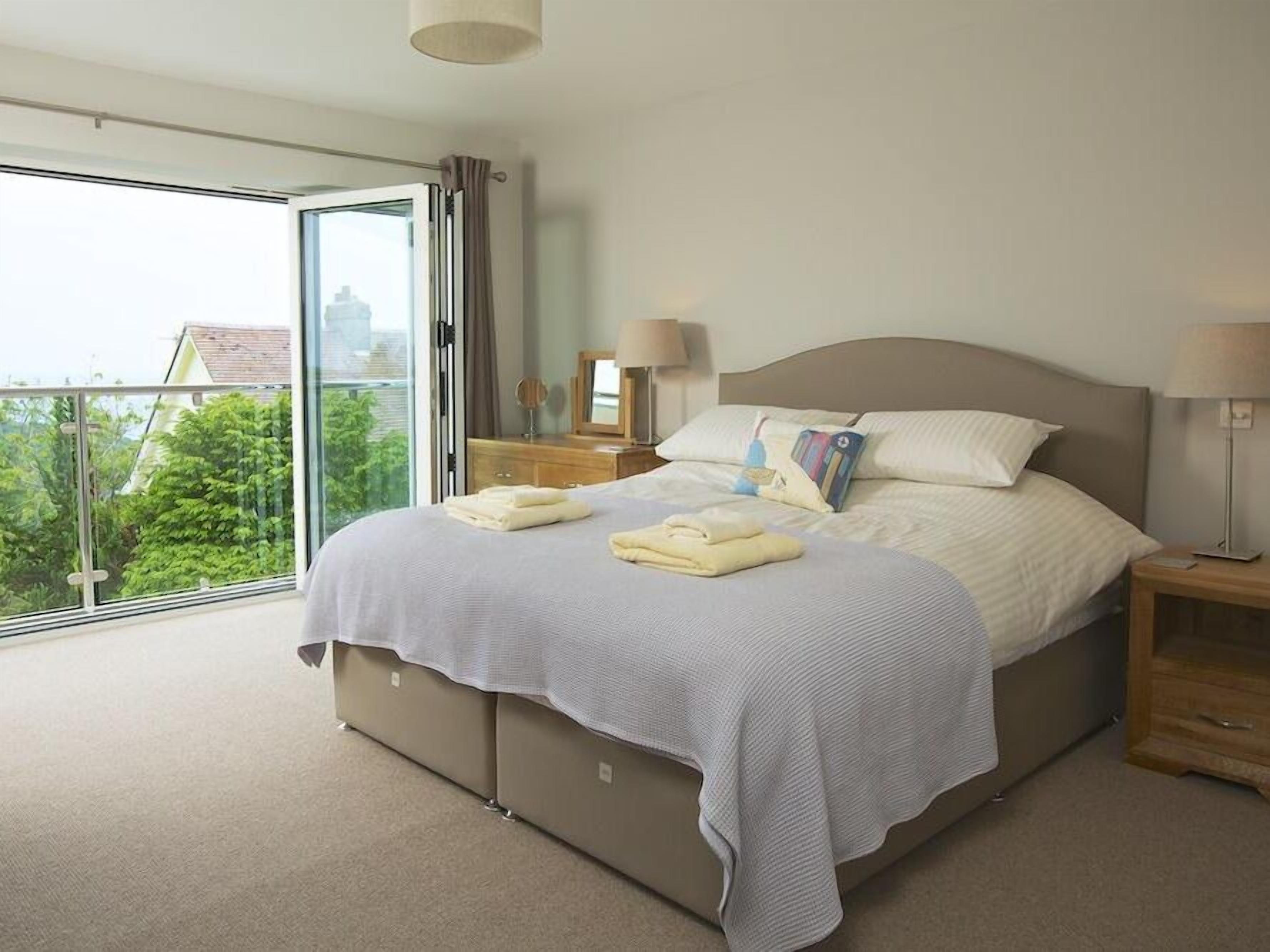 A bedroom with a large bed, two bedside tables, a window with curtains, and a view of greenery outside.