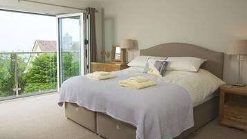 A bedroom with a large bed, two bedside tables, a window with curtains, and a view of greenery outside.