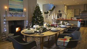 Zona pranzo con un albero di Natale, un camino e una cucina sullo sfondo.