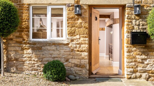 A stone building with a wooden door, a window with a basket inside, and a mailbox on the wall. - Orchard House (Moreton-in-Marsh)