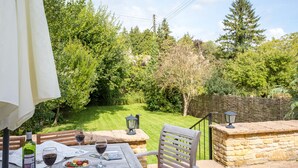 A patio with a table set for two, a bottle of wine, and a bowl of fruit. - Orchard House (Moreton-in-Marsh)