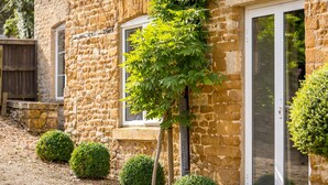 A stone building with a window and a door, surrounded by small bushes. - Orchard House (Moreton-in-Marsh)