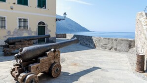 A historic cannon on a wooden carriage, a stone wall, and a building with green shutters. - JOIVY Camogli il Terrazzino e il Mare (Camogli)