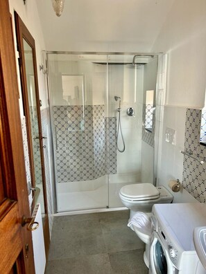 A bathroom with a glass shower enclosure, a toilet, and a washing machine. - JOIVY Camogli il Terrazzino e il Mare (Camogli)