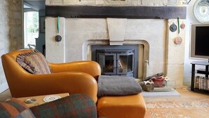 A cozy living room with a stone fireplace, a leather armchair, and a television on a stand. - The Malt House (Burford)