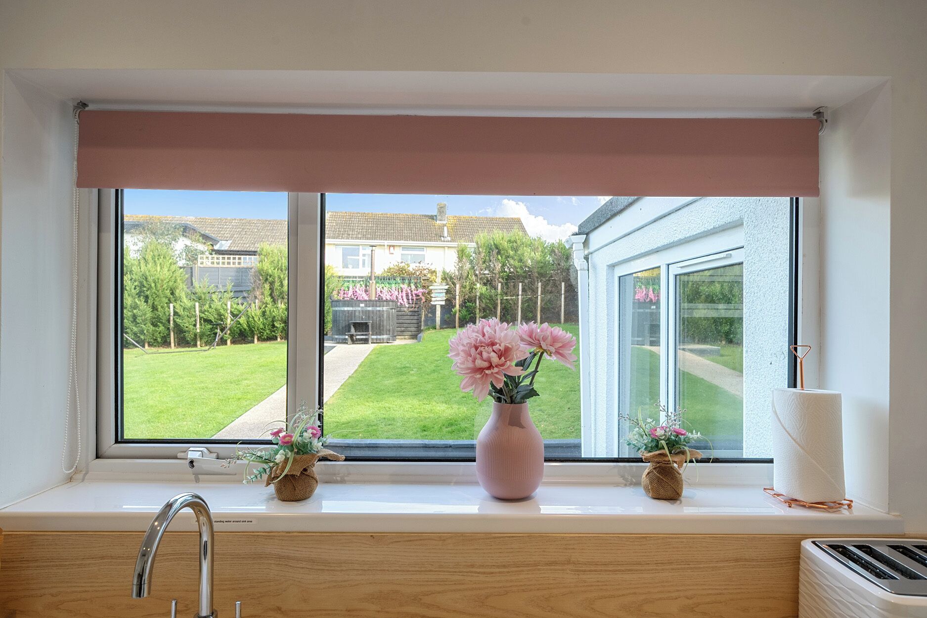 A window with a view of a garden and a house. There are two small vases with flowers on the windowsill.