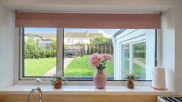 A window with a view of a garden and a house. There are two small vases with flowers on the windowsill.