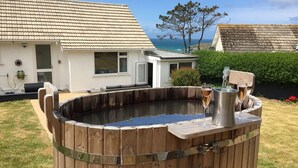A wooden hot tub with a metal container, a white house with a tiled roof, and a view of the sea. - Chi An Mor (Newquay)