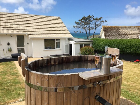 A wooden hot tub with a metal container, a white house with a tiled roof, and a view of the sea. - Chi An Mor (Newquay)