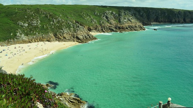 A coastal beach with clear turquoise waters, a sandy shore, and a grassy cliff. - Chi An Mor (Newquay)