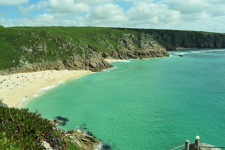 A coastal beach with clear turquoise waters, a sandy shore, and rocky cliffs.