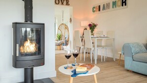 A cozy living room with a wood-burning stove, a dining area with a table set for two, and a sofa. - Chi An Mor (Newquay)