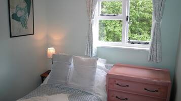 Una camera da letto con un letto, un comodino, una lampada, una cassettiera e una finestra con tende.